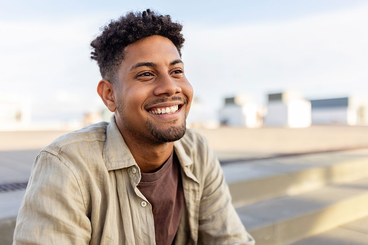 A young African American man smiles as he looks off into the distance on a sunny day