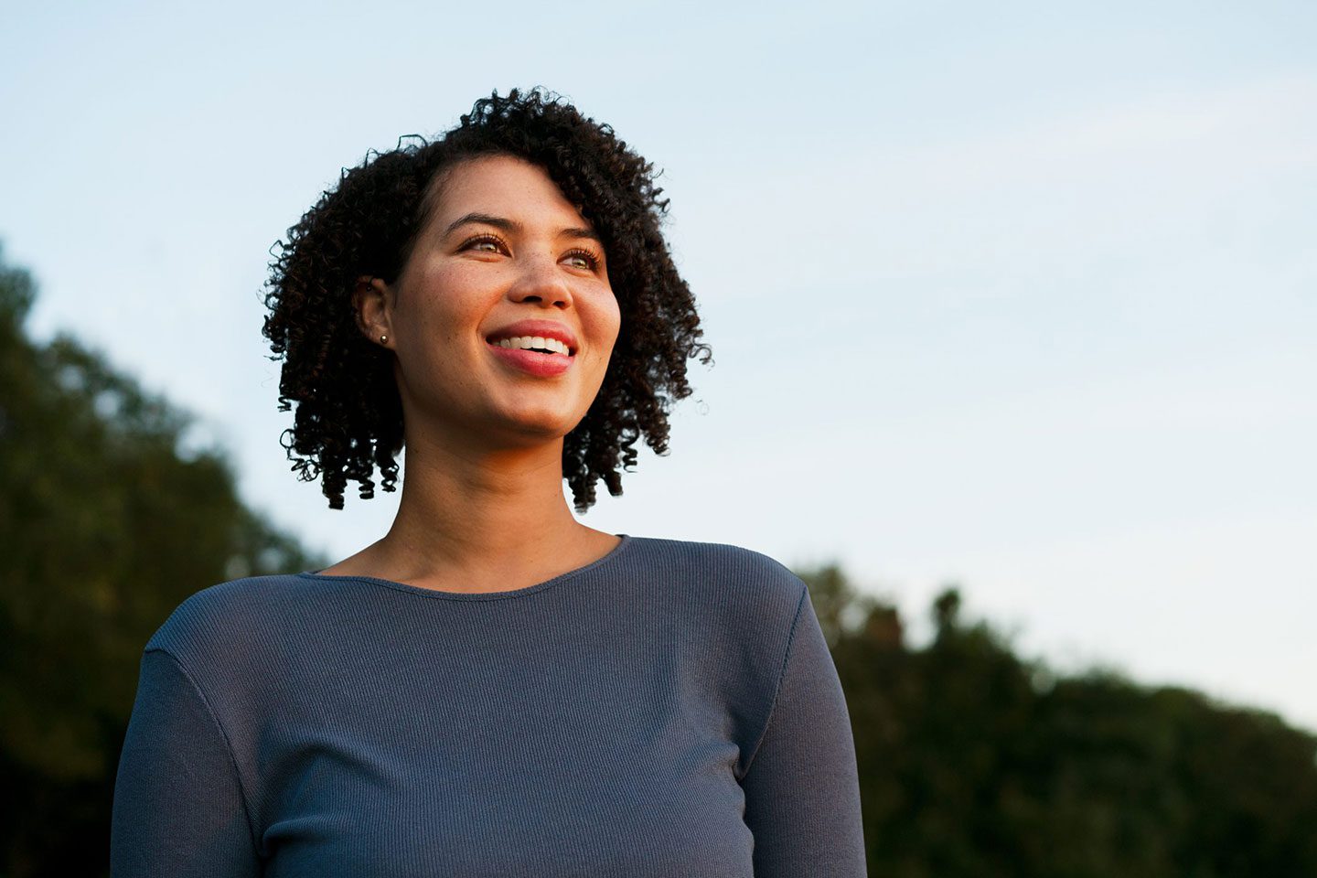 An African American woman smiles as she looks off into the distance, the sun shining on her face